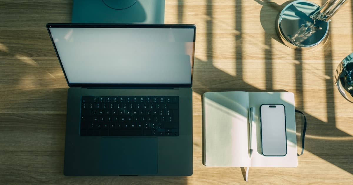 Laptop, Notizbuch und Smartphone auf einem Holzschreibtisch