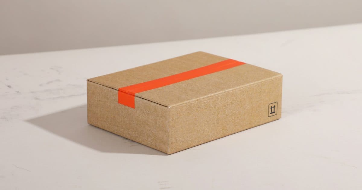 Versandpaket mit orangem Klebeband auf heller Tischplatte, Symbolbild für ein freies Handelsgewerbe