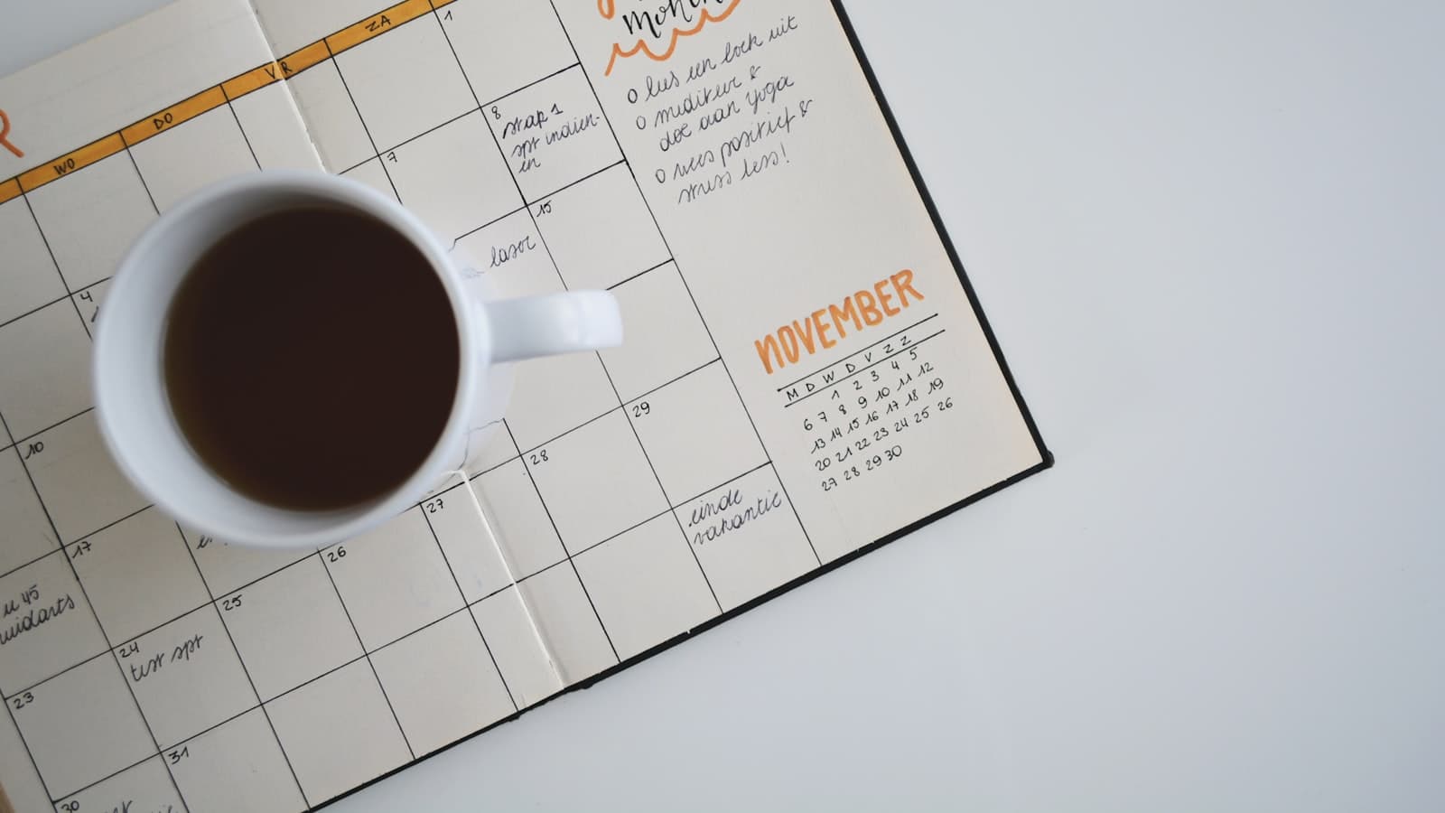 Aufgeschlagener Monatskalender mit einer Tasse Kaffee auf hellem Tisch