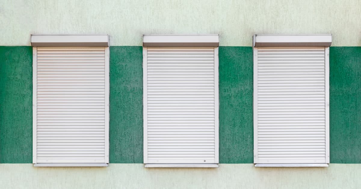 Drei heruntergelassene Rollläden an einer grün gestrichenen Fassade