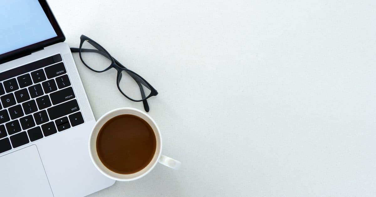 Laptop, Brille und Kaffeetasse auf einem hellen Schreibtisch, Symbolbild für den Gewerbeschein-Antrag online