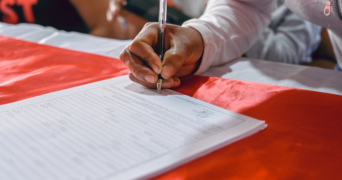 Hand beim Ausfüllen eines Formulars an einem Tisch