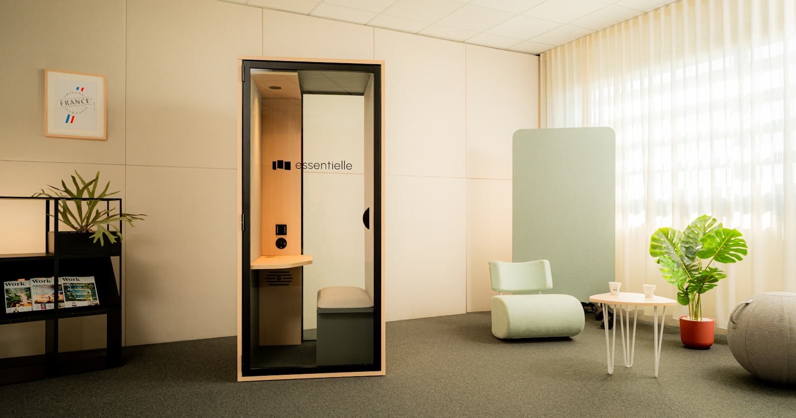 Telefonbox mit Glastür und Holzinnenraum in einem hellen Büro neben einer Sitzecke