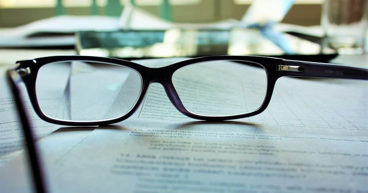 Lesebrille auf einem ausgedruckten Formular, im Hintergrund weitere Unterlagen auf einem Schreibtisch